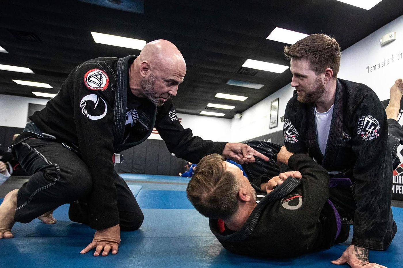 Brent Lillard, in a black gi, coaching two students on the mat at Gracie Charlottesville